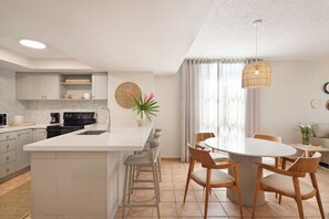 A modern kitchen with a central island, bar stools, and a dining table with chairs.