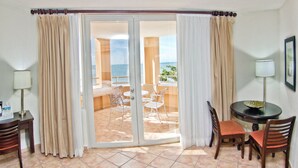 A hotel room with a sliding glass door leading to a balcony with a view of the sea. There is a small table with chairs and a lamp on the balcony. - Rincon Beach Resort (Añasco)