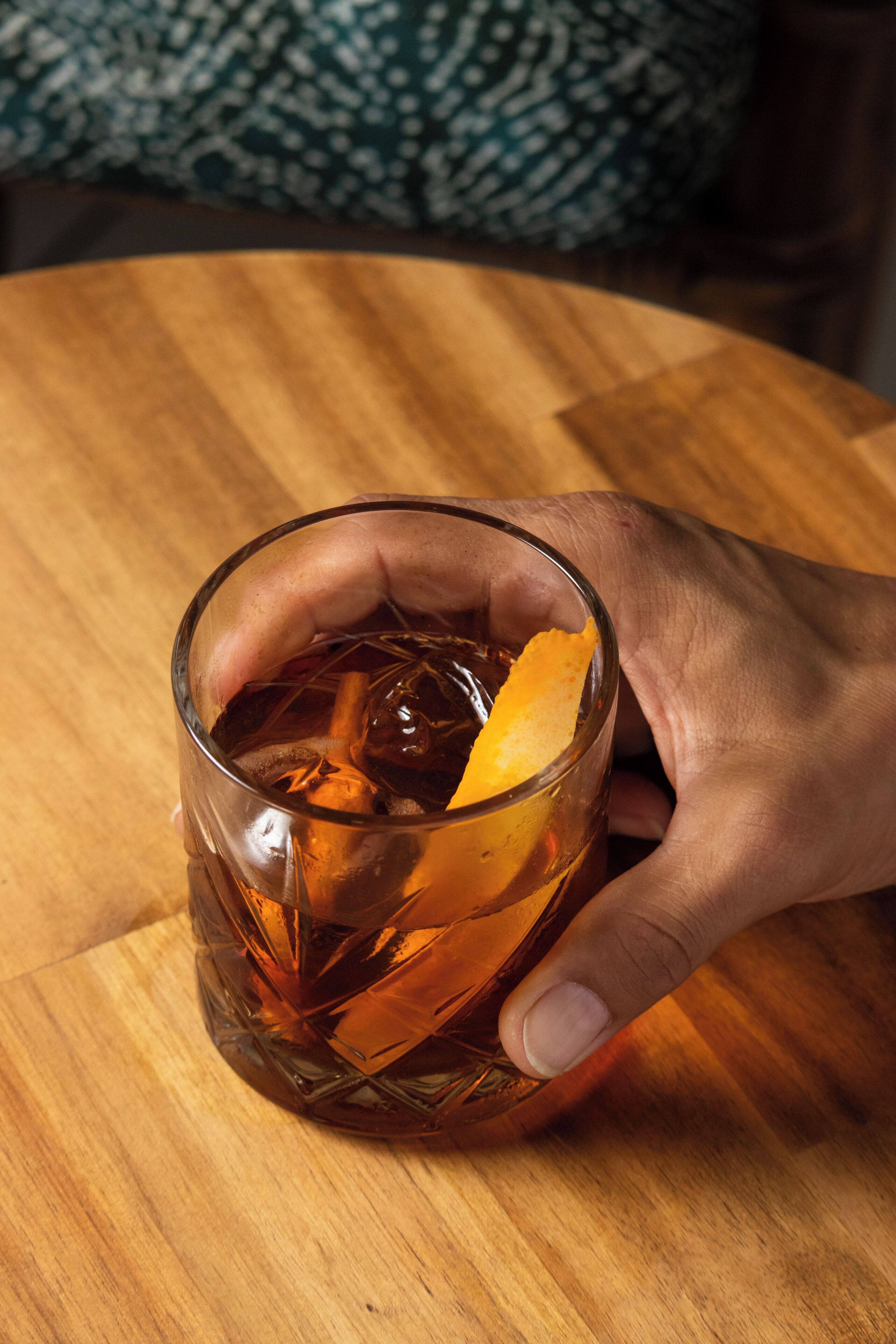 A hand holding a glass with ice cubes and a slice of orange.