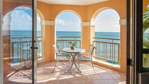 A balcony with a table and chairs, a view of the sea, and a tropical plant. - Rincon Beach Resort (Añasco)