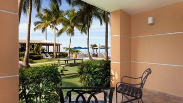 A balcony with a view of a pool area, palm trees, and a building with a covered seating area.