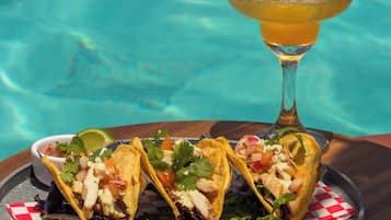 A table with two tacos and a cocktail by a pool.