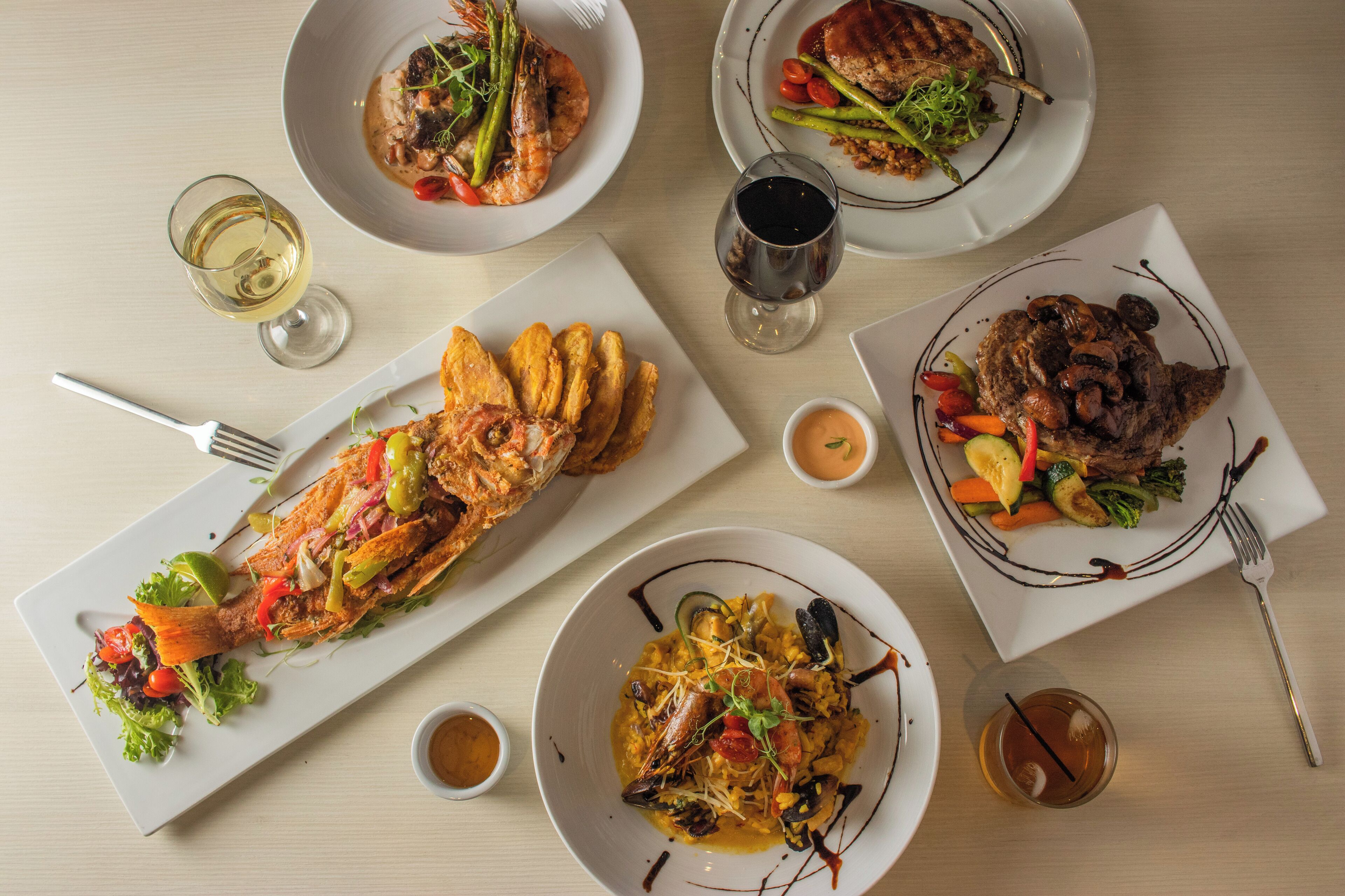 Une table dressée avec divers plats, notamment des fruits de mer, des légumes et de la viande, accompagnée de verres de vin.