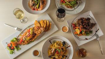 Une table dressée avec divers plats, notamment des fruits de mer, des légumes et de la viande, accompagnée de verres de vin.