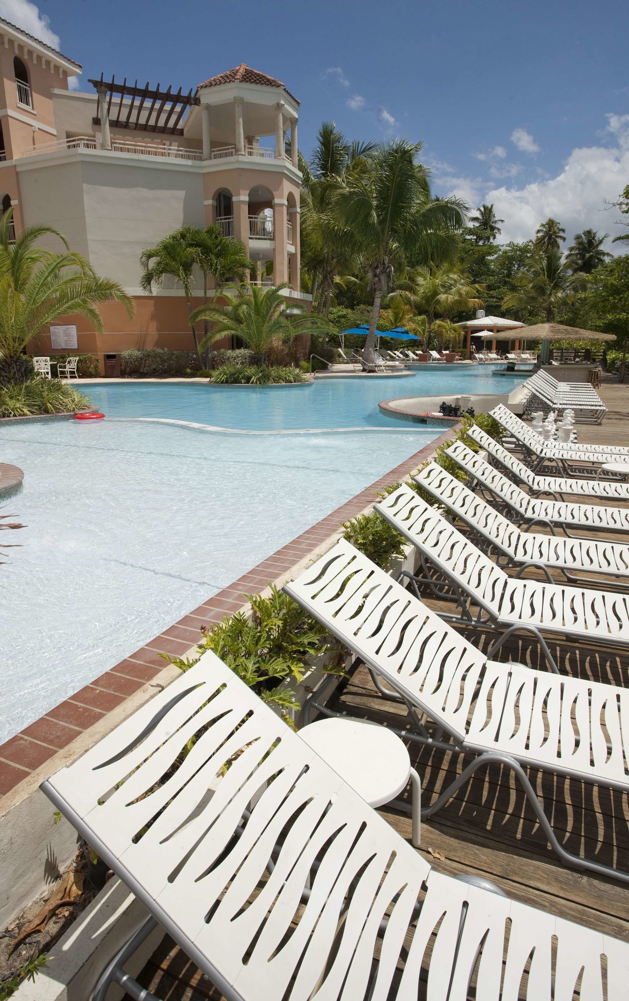 Un espace piscine avec des chaises longues et un bâtiment doté d’un balcon.