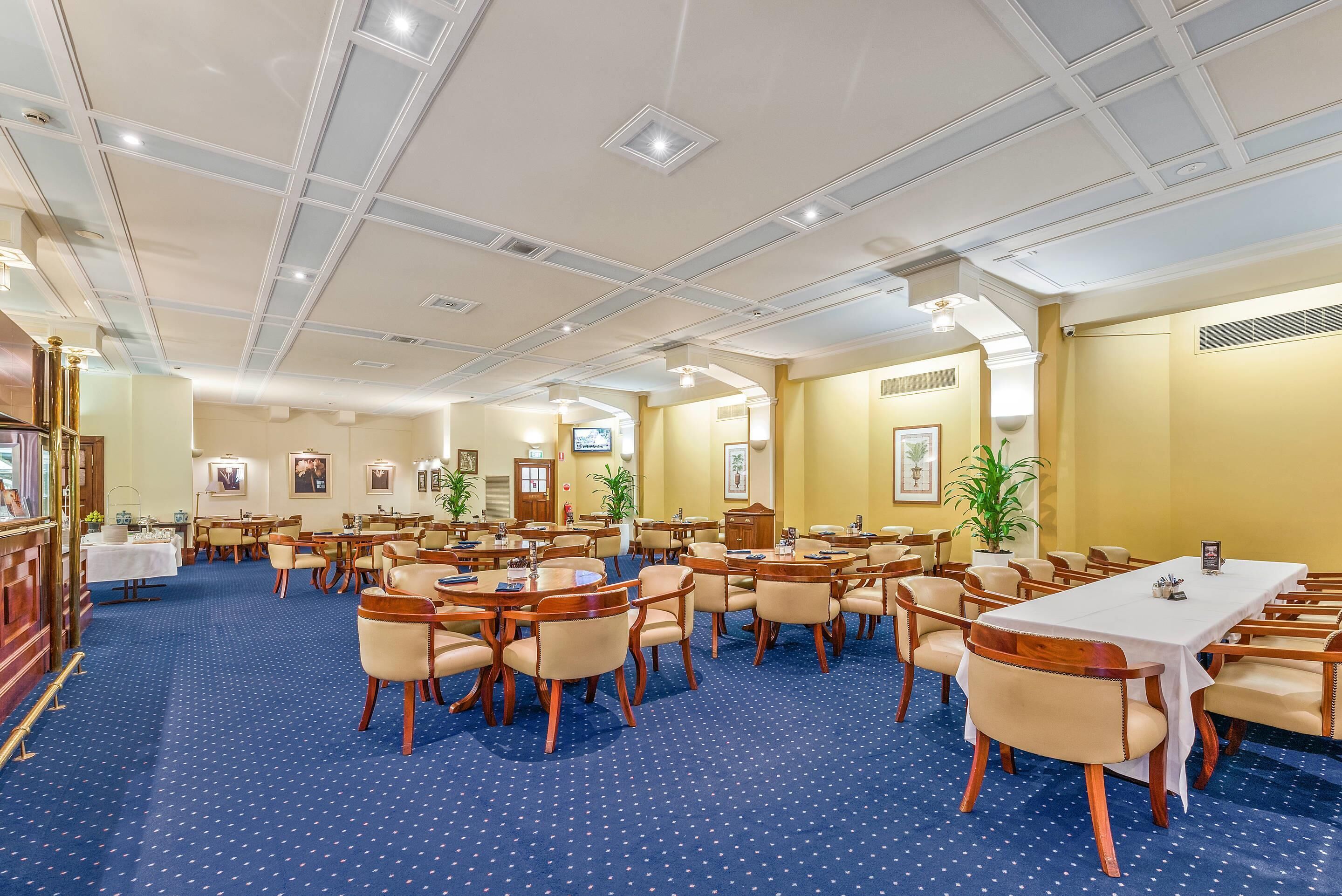 Un salón de conferencias de hotel con varias mesas y sillas, una alfombra azul y un techo blanco con iluminación empotrada.