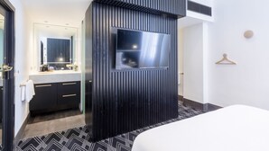 A modern hotel room with a black accent wall, a large mirror, a flat-screen TV, a bed, and a wooden hanger on the wall. - Castlereagh Boutique Hotel, an Ascend Collection Hotel (Sydney)