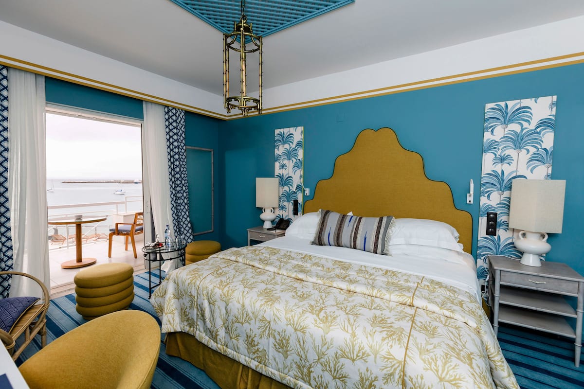 A hotel room with a large bed, a view of the sea, a balcony, and a modern chandelier.