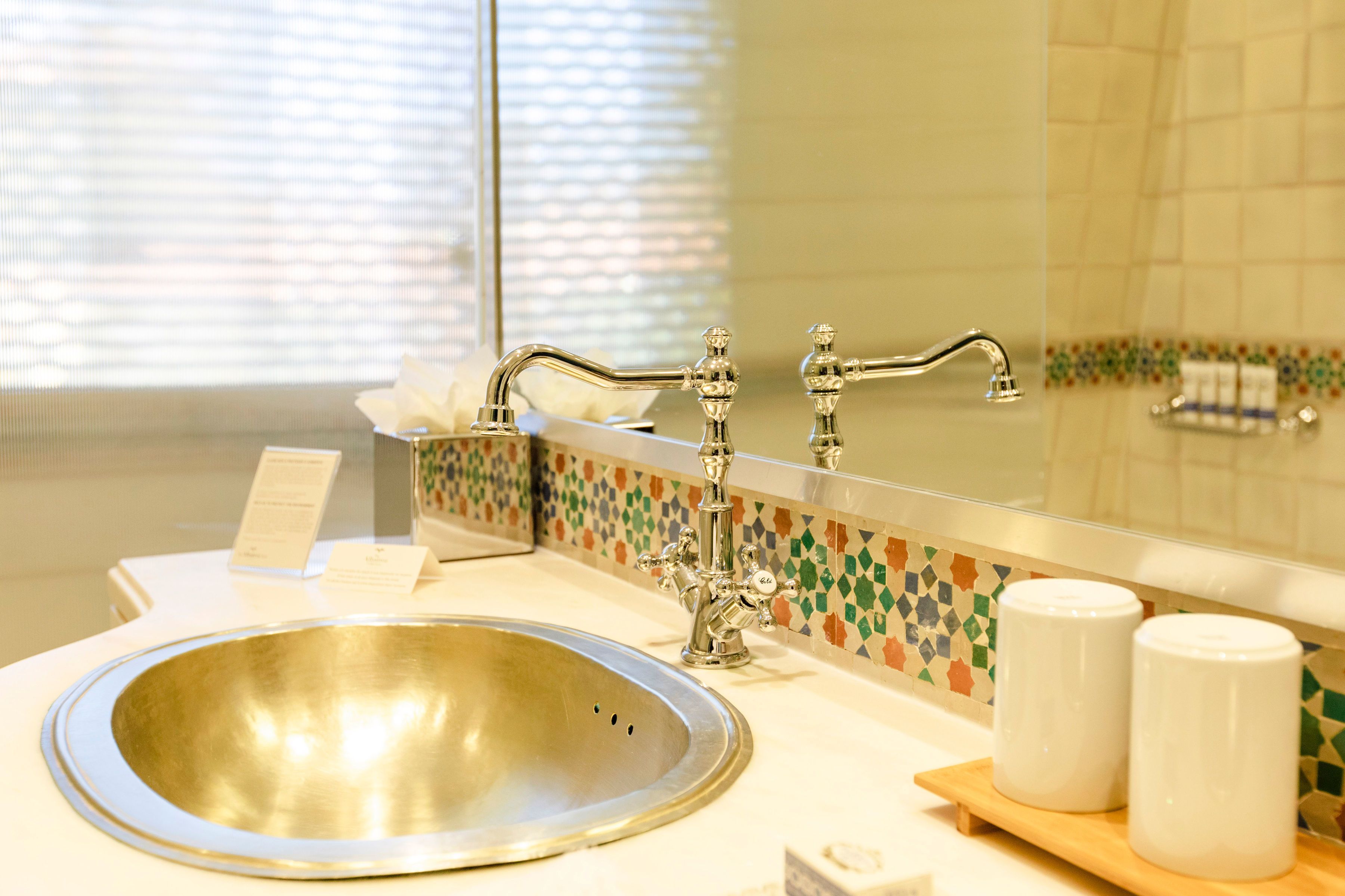 Un baño con un lavamanos, dos botellas blancas, un espejo y un salpicadero de azulejos.