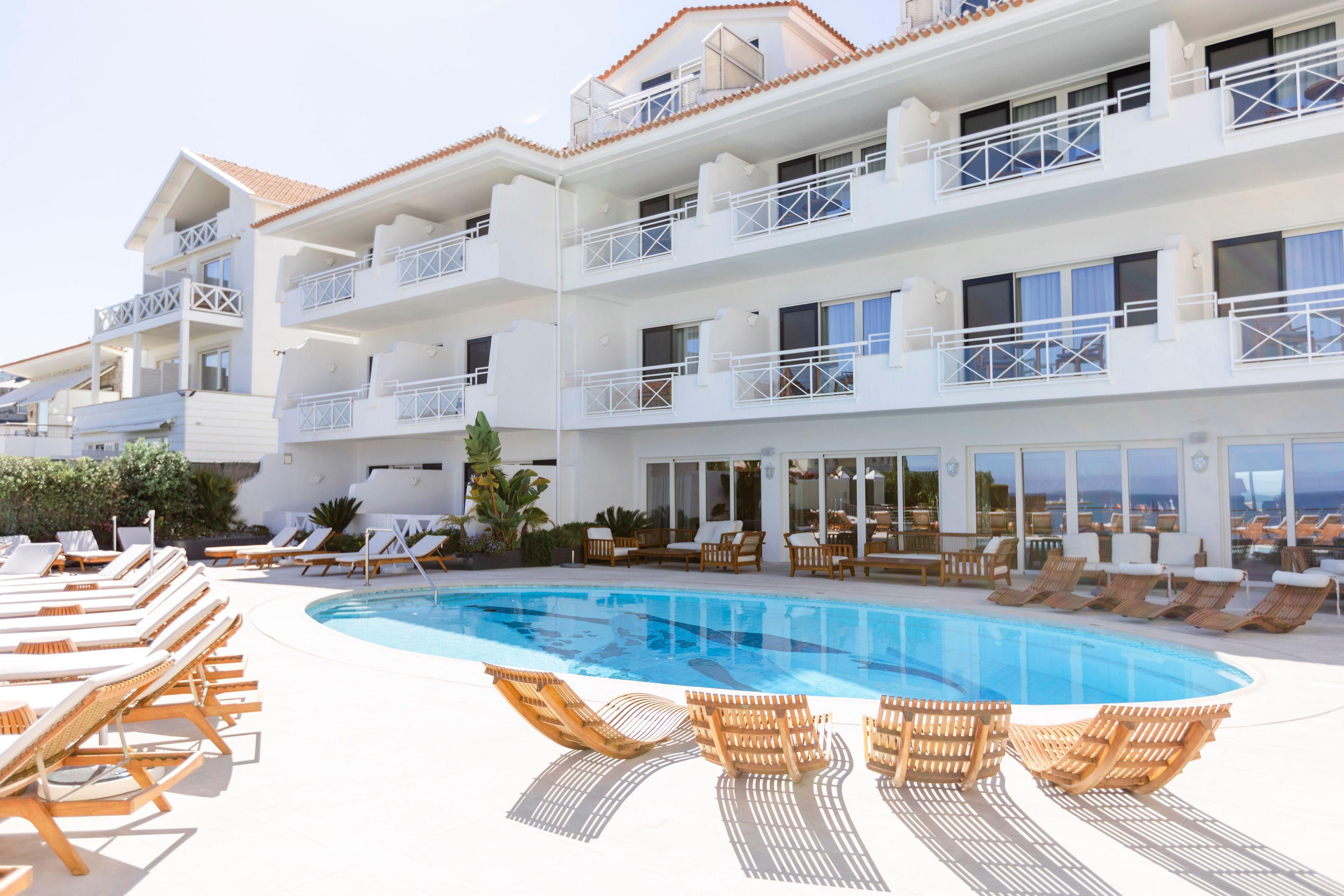 A multi-story hotel with a swimming pool, sun loungers, and a terrace with a view.