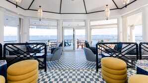 A spacious deck with checkered flooring, seating arrangements, and large windows offering a view of the sea. - The Albatroz Hotel (Cascais)