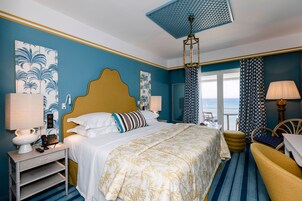 Una habitación de hotel con cama, mesita de noche, lámpara y vista al mar.