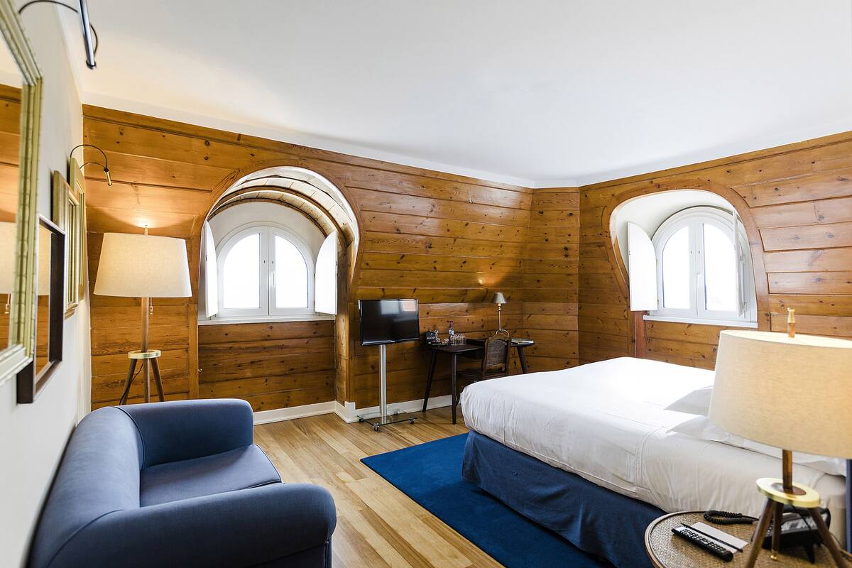A hotel room with wooden walls, a bed, a desk, a chair, and a TV.