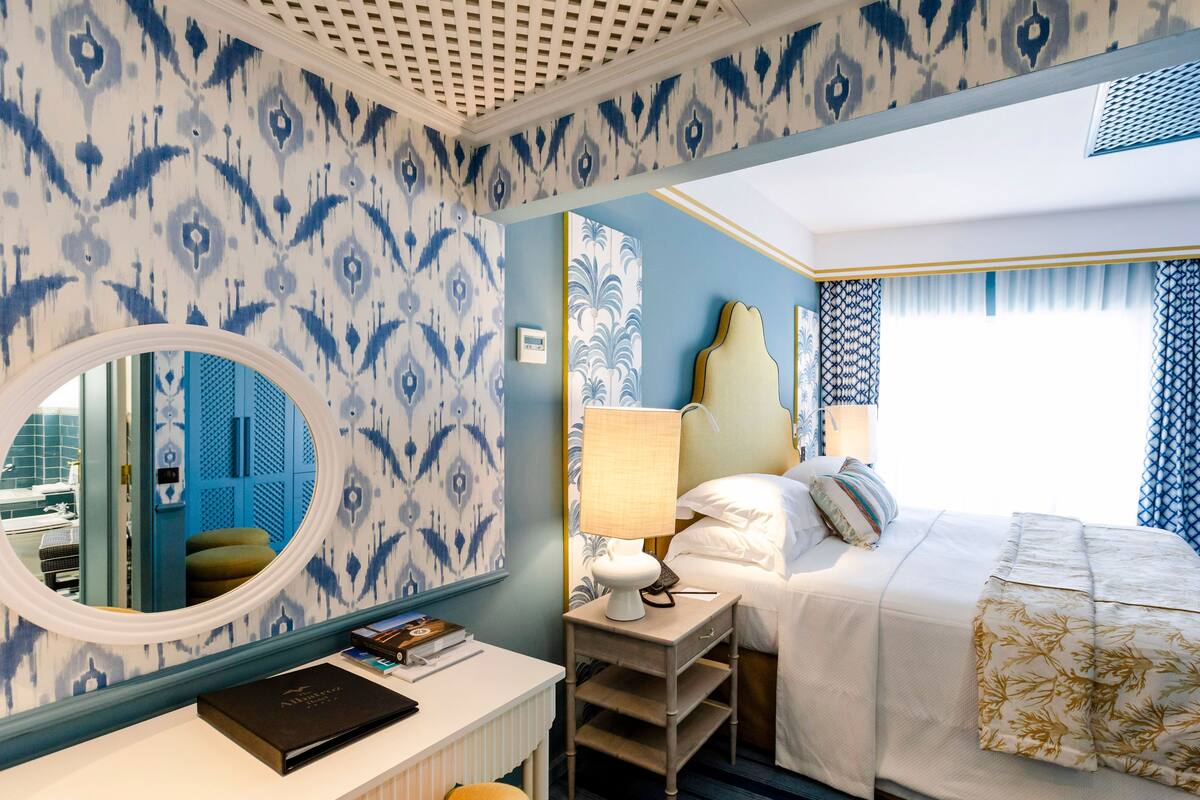 A hotel room with a bed, bedside table, lamp, and a mirror.