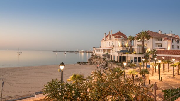 A beachfront hotel with a large building, a sandy beach, and calm sea. - The Albatroz Hotel (Cascais)
