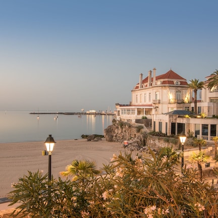 A beachfront hotel with a large building, a sandy beach, and calm sea.