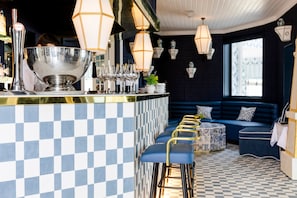 A bar area with checkered tile flooring, bar stools, and hanging light fixtures.