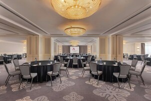 Un salón de conferencias con mesas redondas, sillas y una gran lámpara de araña.