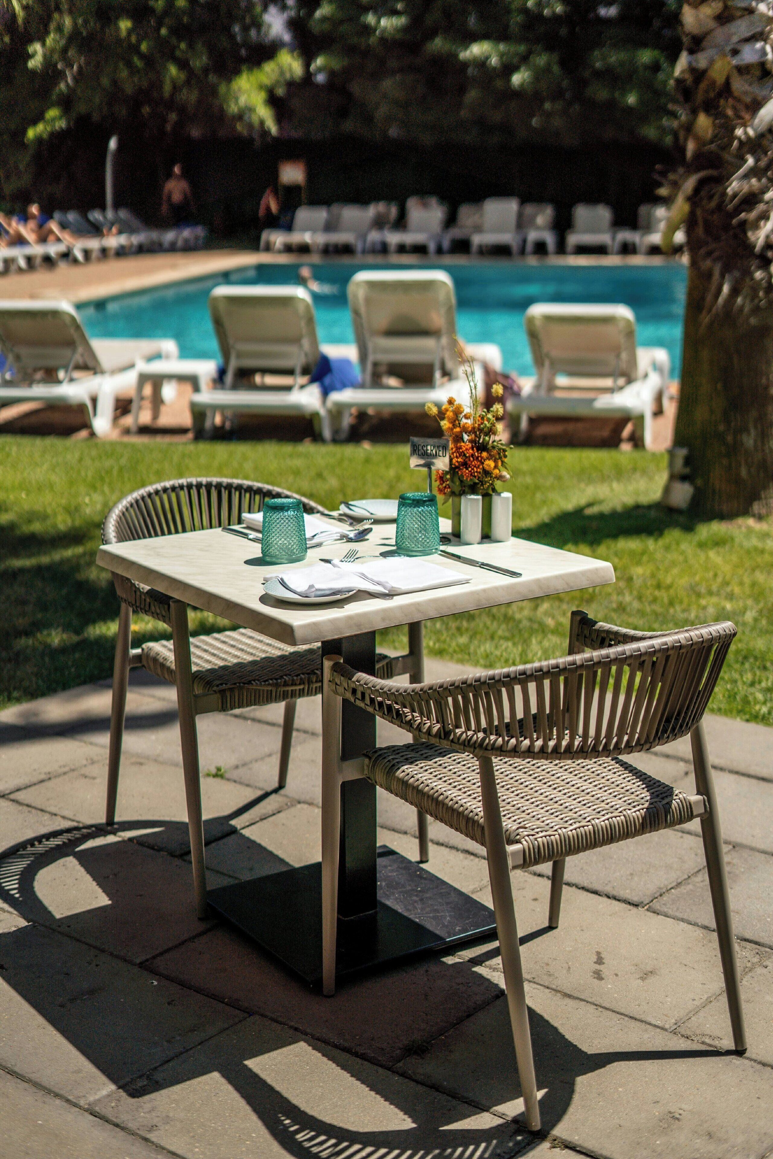 A dining table with chairs, a pool, and lounge chairs in the background.