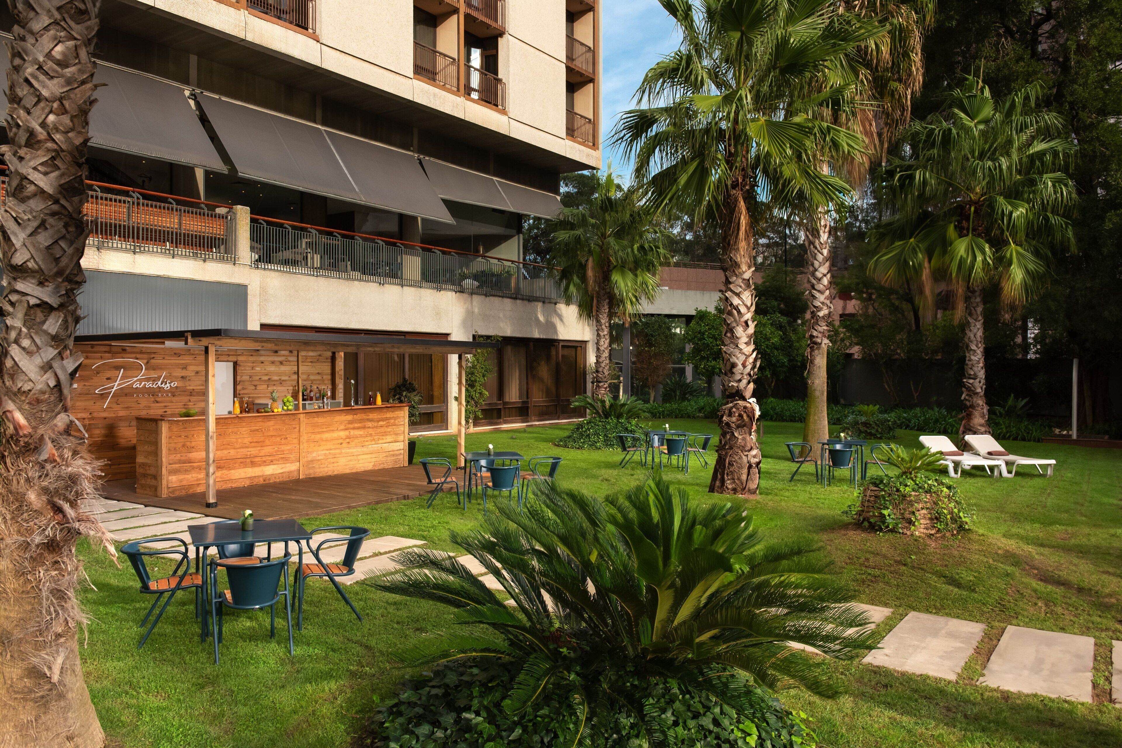 A hotel with a bar area, outdoor seating, and palm trees.