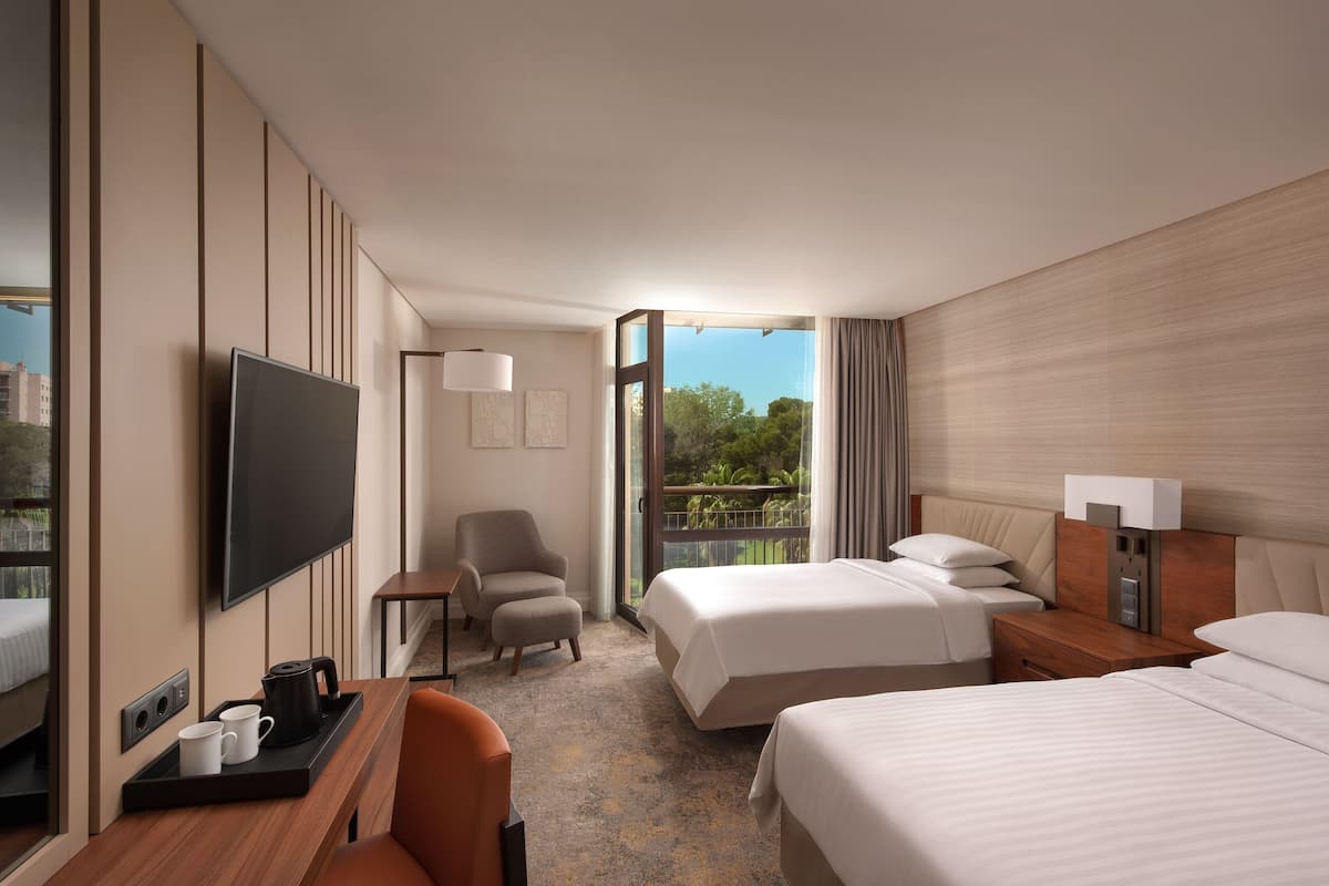 A hotel room with two beds, a TV, a desk with a coffee pot, and a chair.