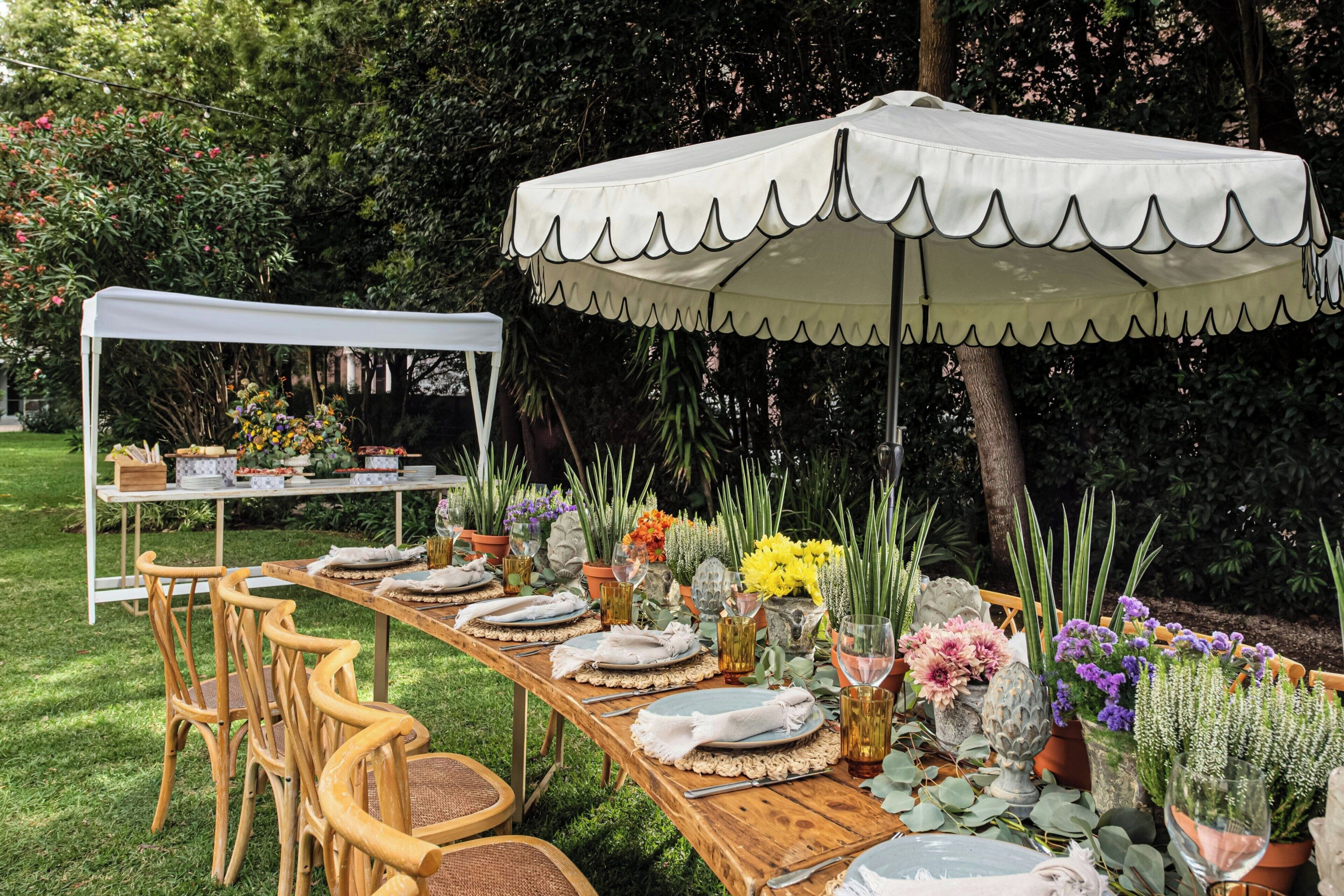 An outdoor dining setup with a long wooden table, white chairs, and a white canopy tent.