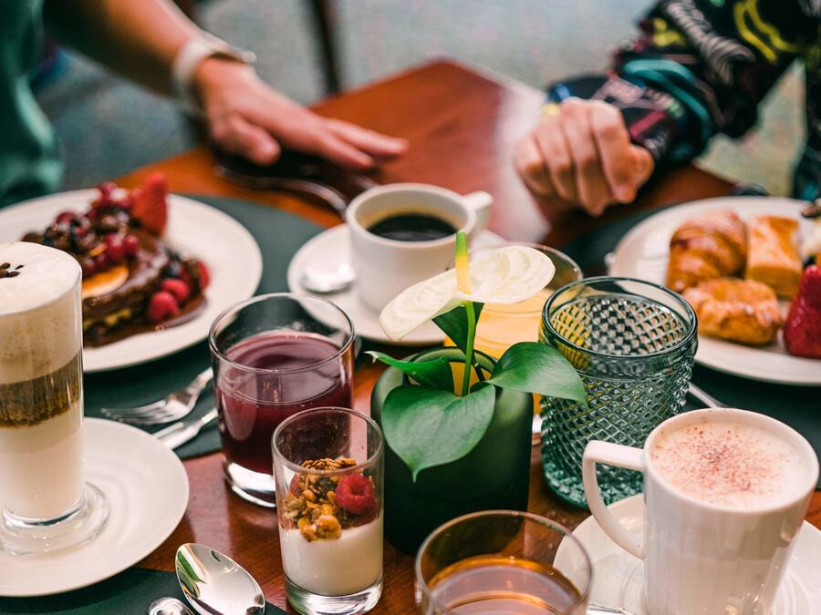Une table à manger avec divers aliments et boissons, notamment une assiette de pâtisseries, un verre de lait et une tasse de café.