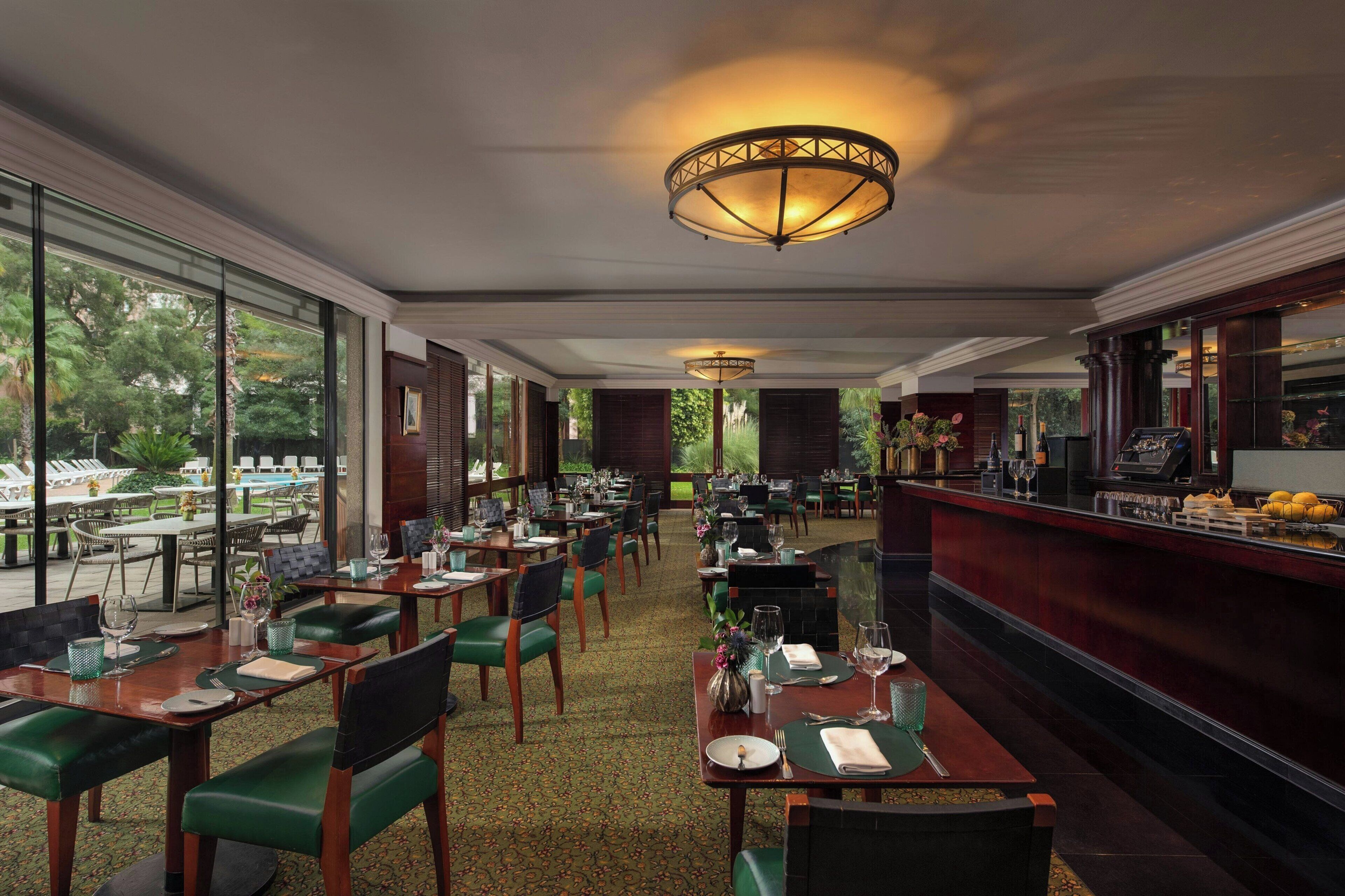 A restaurant with tables set for dining, a bar area, and large windows offering a view of the outdoors.