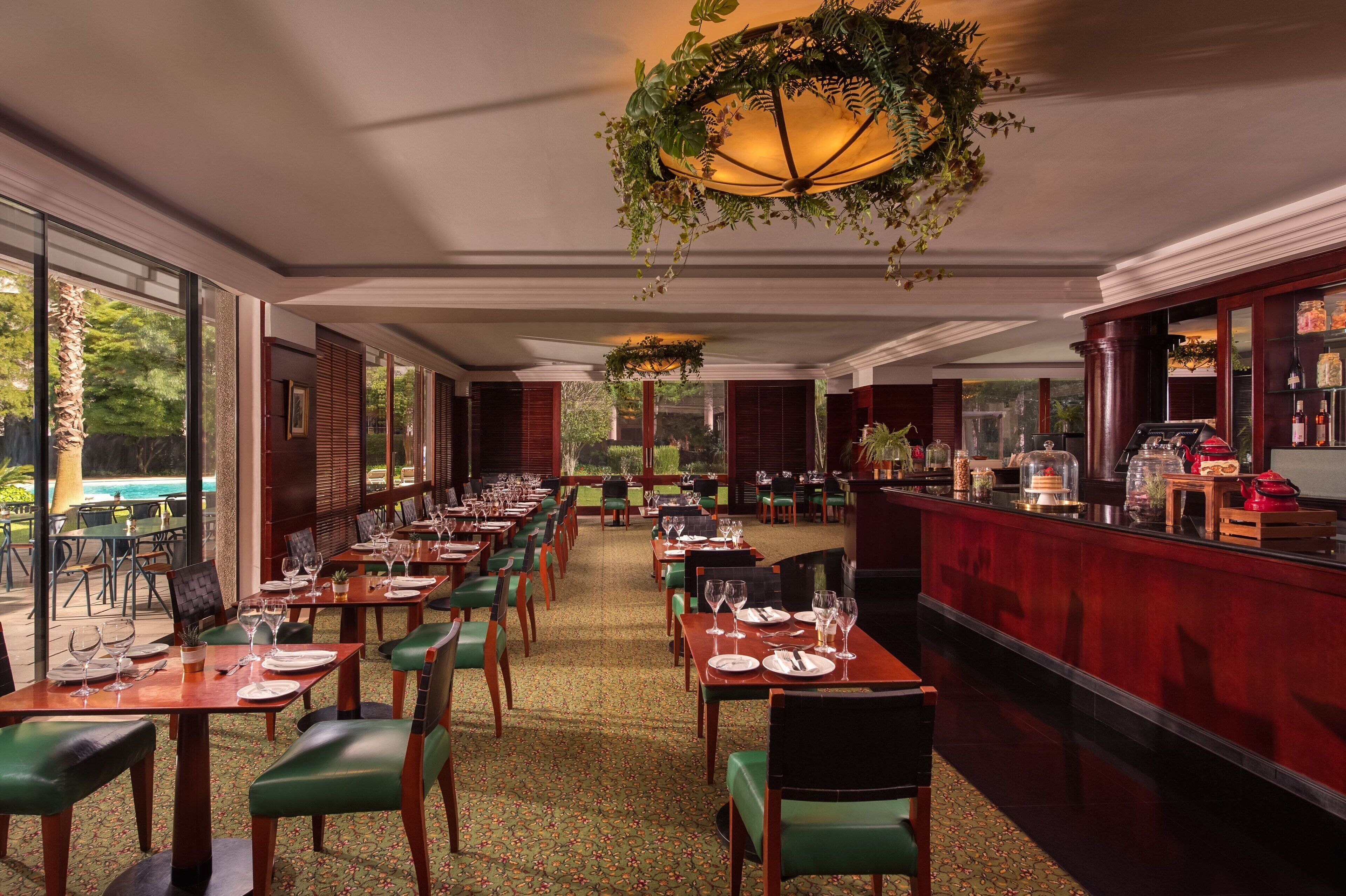 A restaurant with long tables, green chairs, and a bar area.