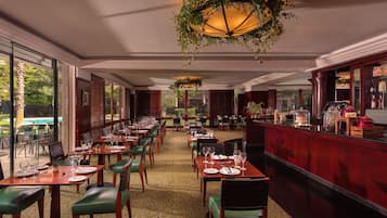 A restaurant with long tables, green chairs, and a bar area.