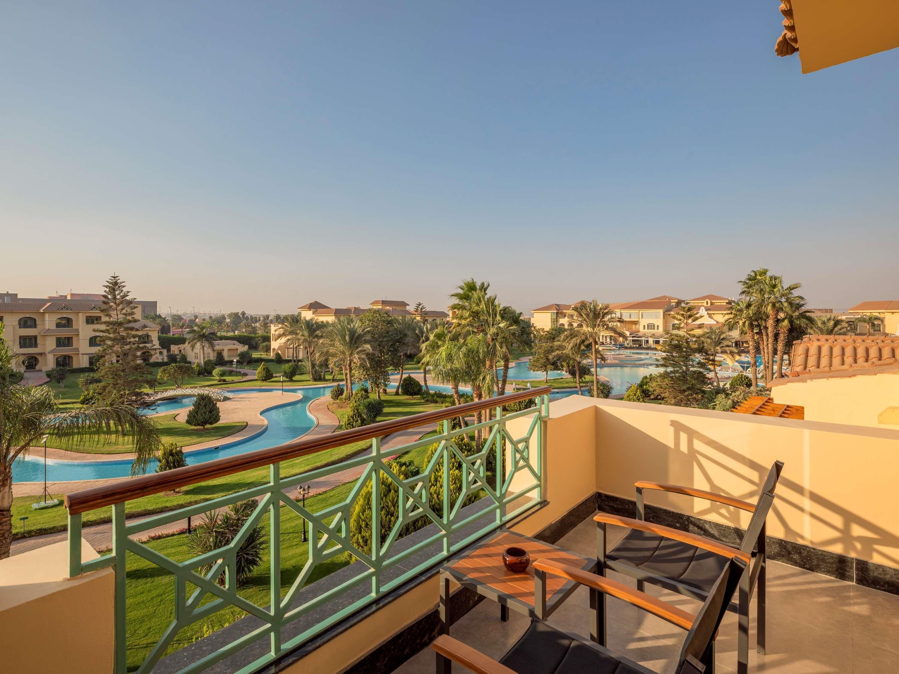 Un balcon avec vue sur une piscine, des palmiers et les bâtiments de l’hôtel.