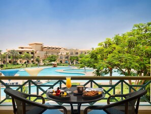 A balcony with a table set for breakfast, overlooking a pool and resort buildings. - Mövenpick Cairo Media City (6th of October City)