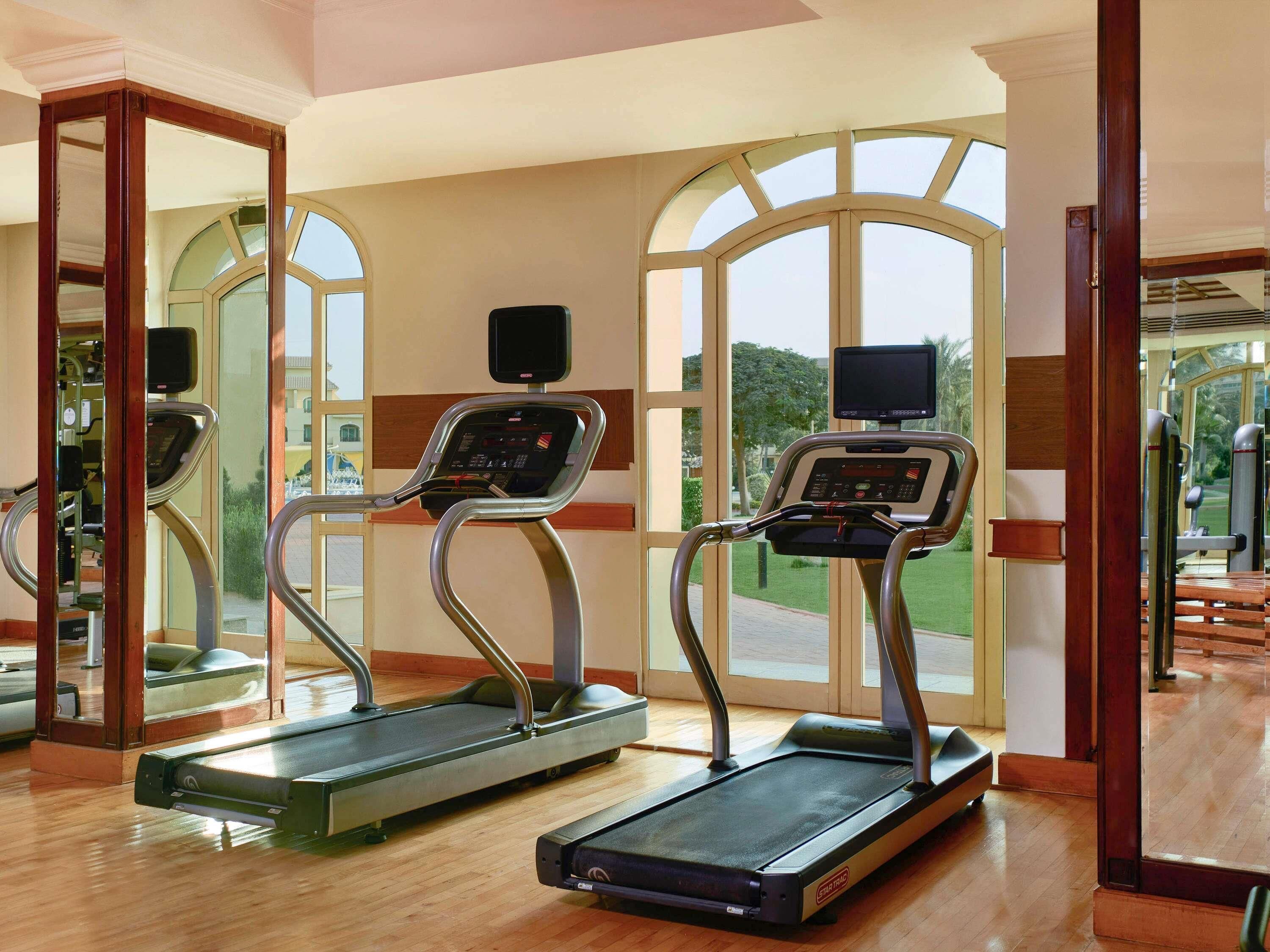 A gym with two treadmills, large windows, and a wooden floor.