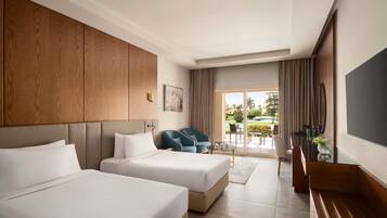 Habitación de hotel con dos camas, televisión, escritorio y vista a un campo de golf a través de la puerta corrediza de vidrio.