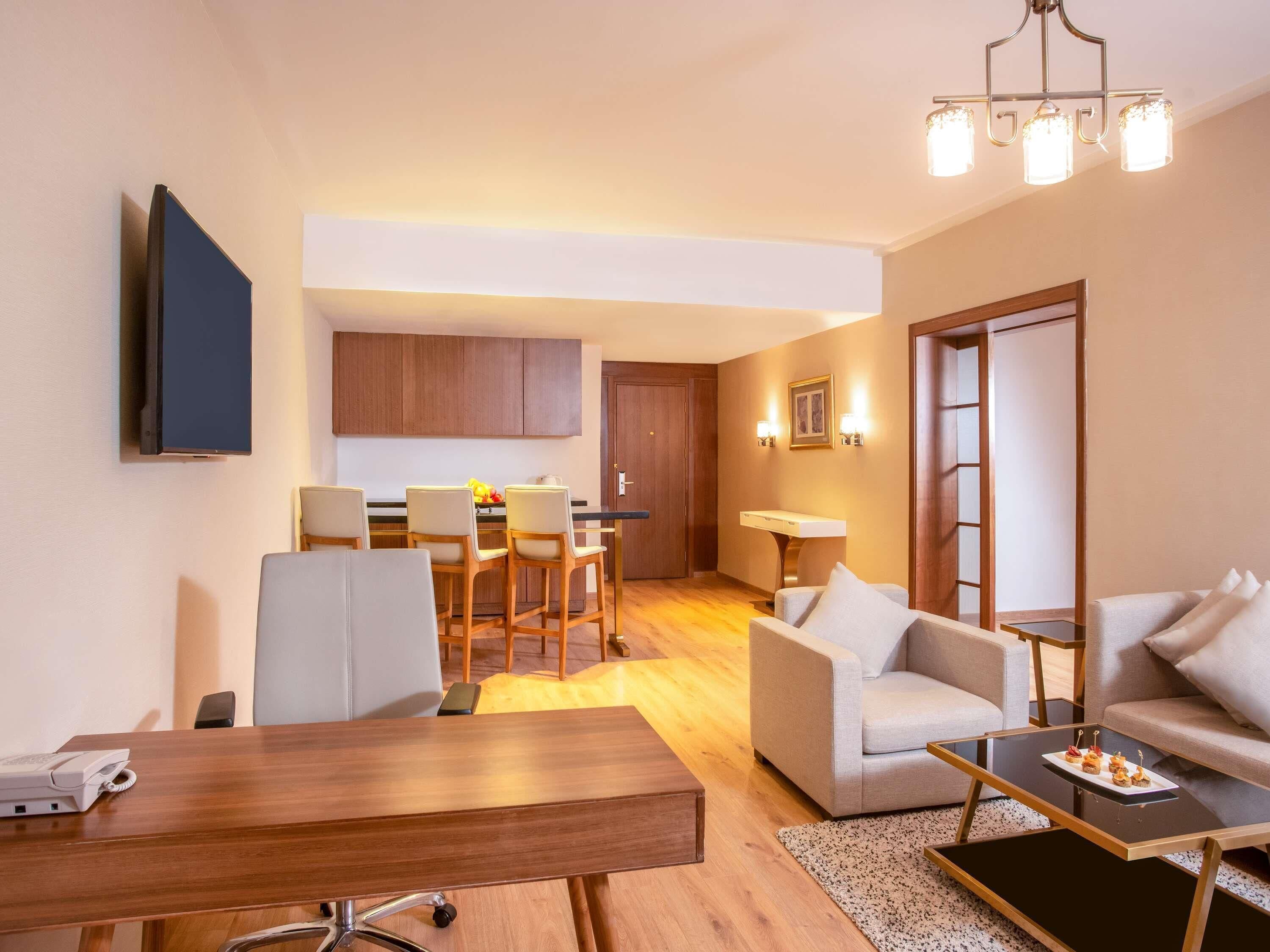 Uma sala de estar moderna com uma mesa de jantar de madeira, dois sofás, uma mesa de centro e uma cozinha ao fundo.