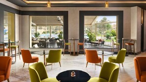 A modern interior with a central round table surrounded by chairs, large windows offering views of outdoor seating, and a ceiling with recessed lighting. - Mövenpick Cairo Media City (6th of October City)