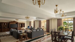 A spacious living room with a large sofa, a television, and a dining area with a table and chairs. - Mövenpick Cairo Media City (6th of October City)