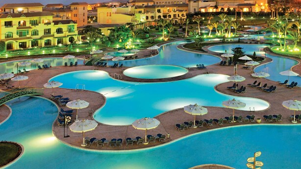 A resort with multiple interconnected swimming pools, sun loungers, and umbrellas. - Mövenpick Cairo Media City (6th of October City)
