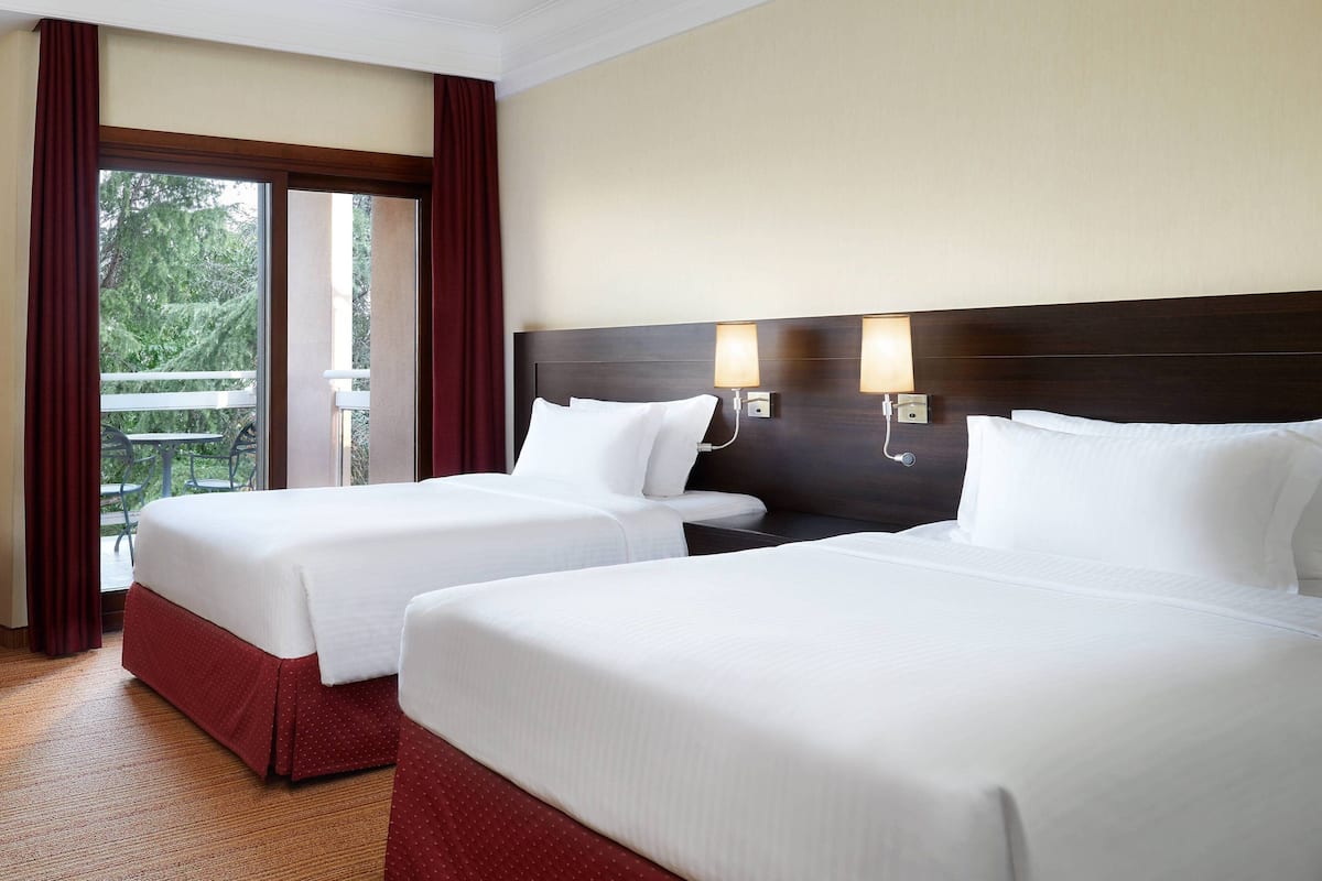 A hotel room with two beds, a balcony, and a view of the outdoors.