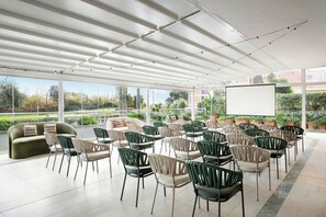 A conference room with a large screen, rows of chairs, and a sofa. - Courtyard by Marriott Rome Central Park (Rome)
