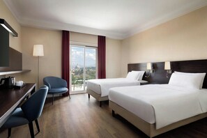 Habitación de hotel con dos camas, un escritorio, una silla y vistas a una estructura en forma de cúpula a través de una ventana.