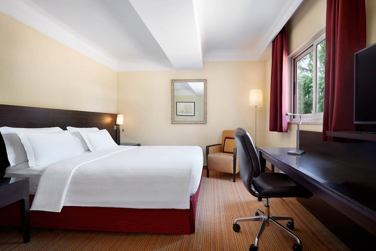 A hotel room with a large bed, a desk, a chair, a TV, and a window with curtains.
