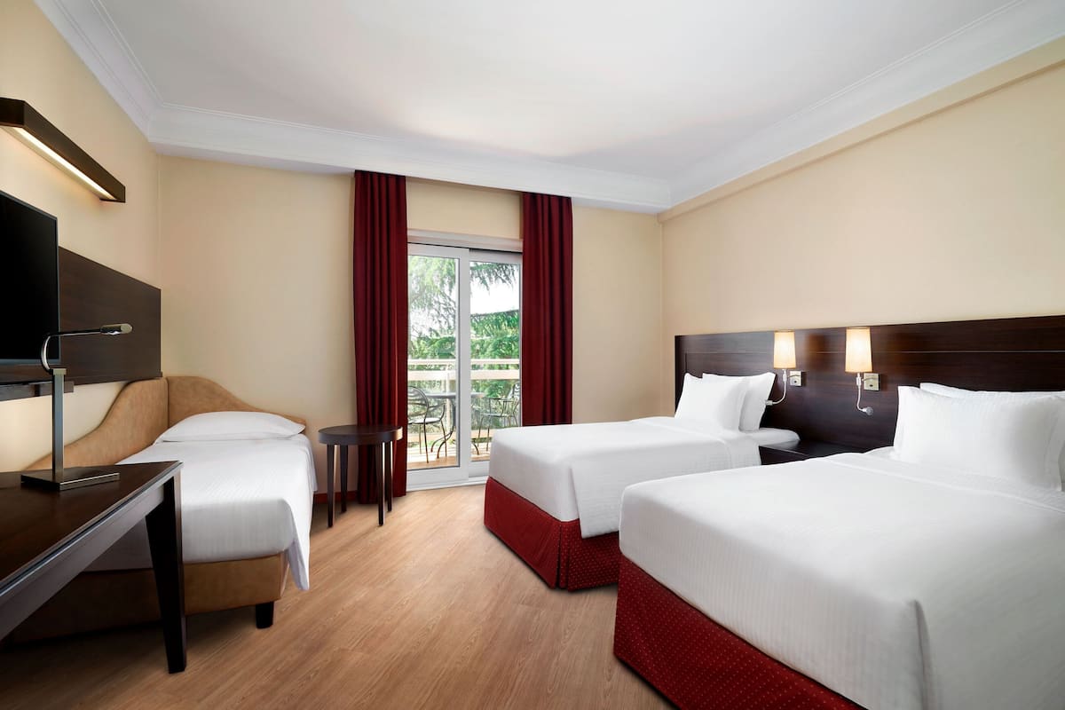 A hotel room with two beds, a desk, a chair, a TV, and a balcony with red curtains.