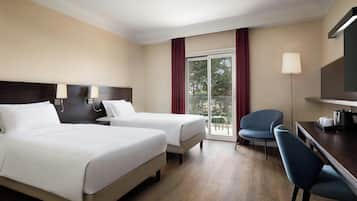 A hotel room with two beds, a desk with a chair, a television, and a view of the outdoors through a window.