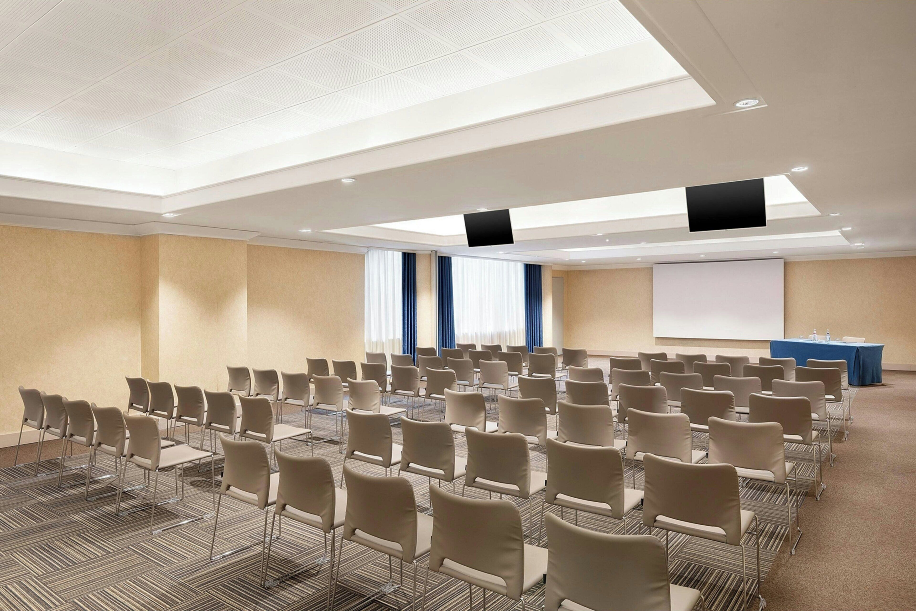 Ein Konferenzraum mit Reihen von Stühlen, einer Projektionsleinwand und einem Rednerpult.