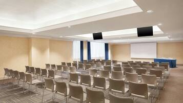Ein Konferenzraum mit Reihen von Stühlen, einer Projektionsleinwand und einem Rednerpult.