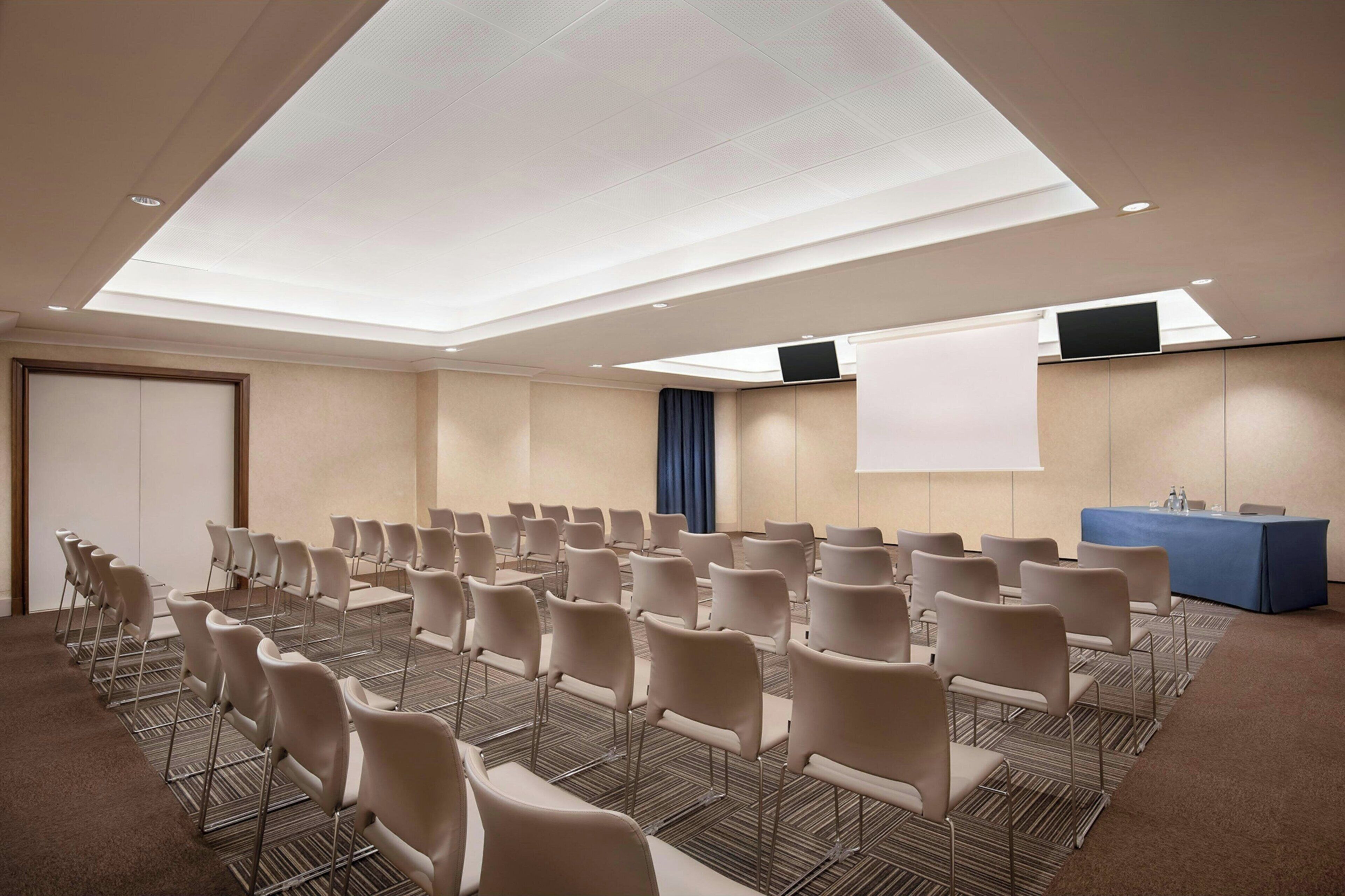 A conference room with rows of chairs, a large screen, and a projection screen.