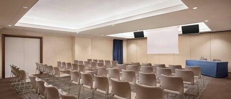 A conference room with rows of chairs, a large screen, and a projection screen.