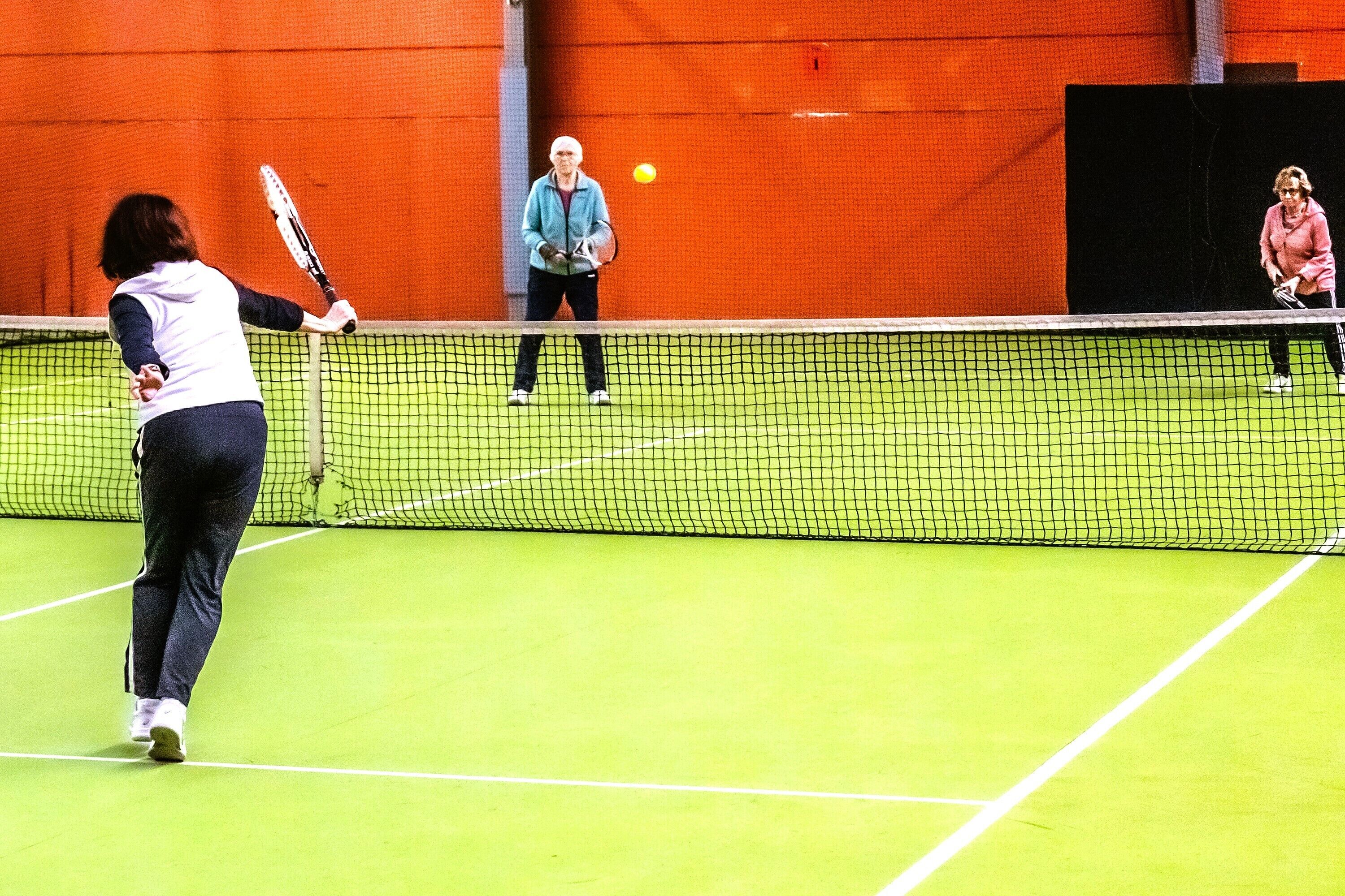 Una cancha de tenis con una red en el centro, rodeada de muros anaranjados.