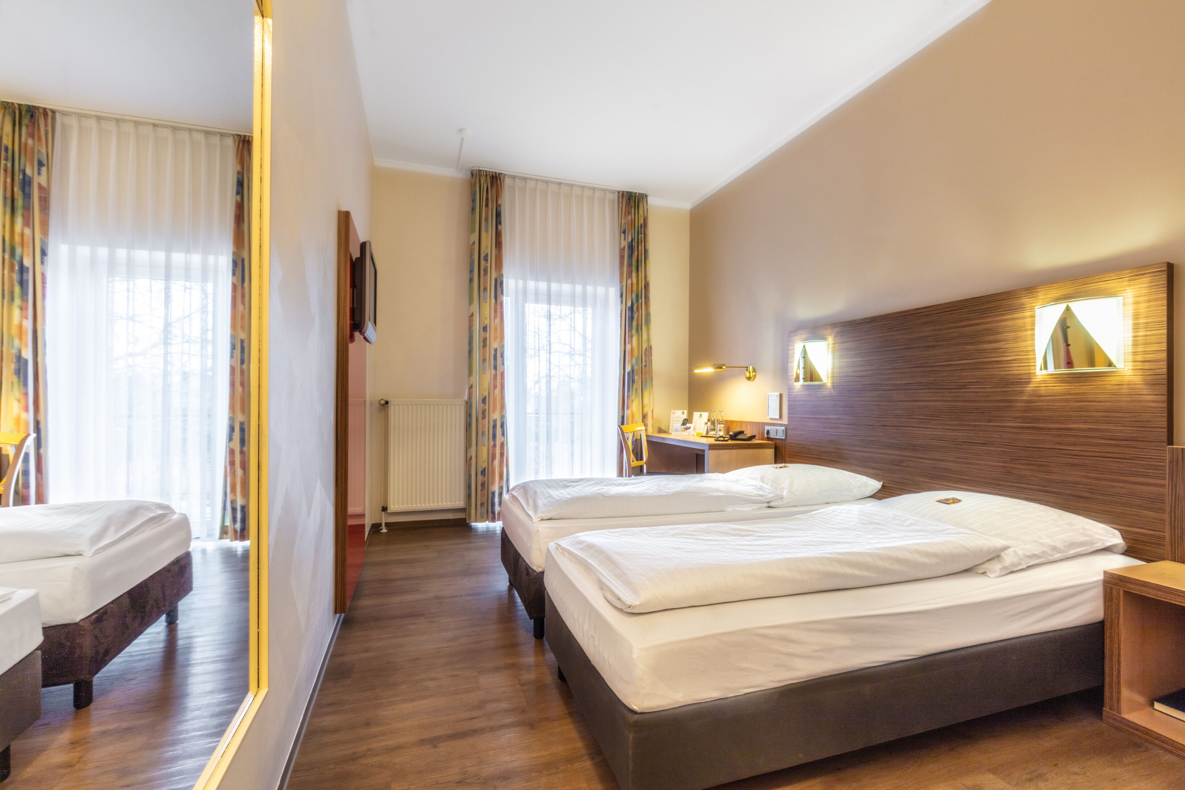 A hotel room with two beds, a desk, and a mirror.